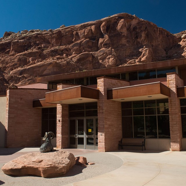 a tan building with high red-rock cliffs in the background