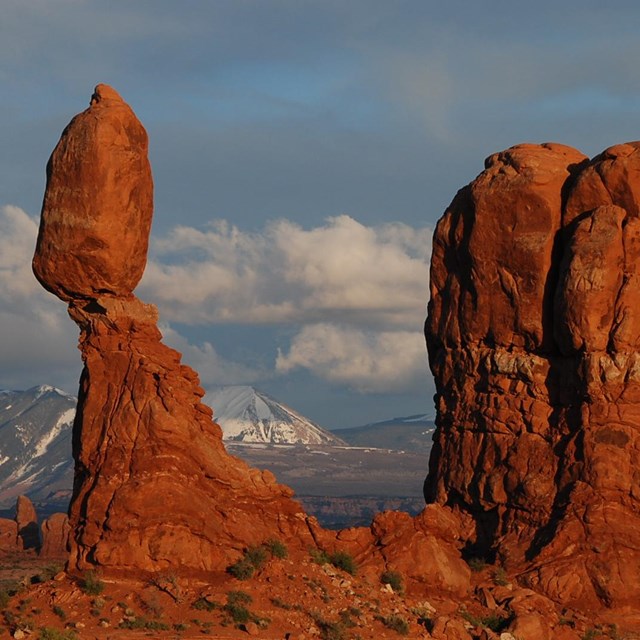 a balanced rock with snow-capped mountains in the distance