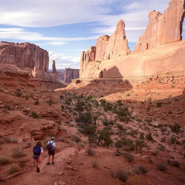people walk on a trail beneath high cliff walls