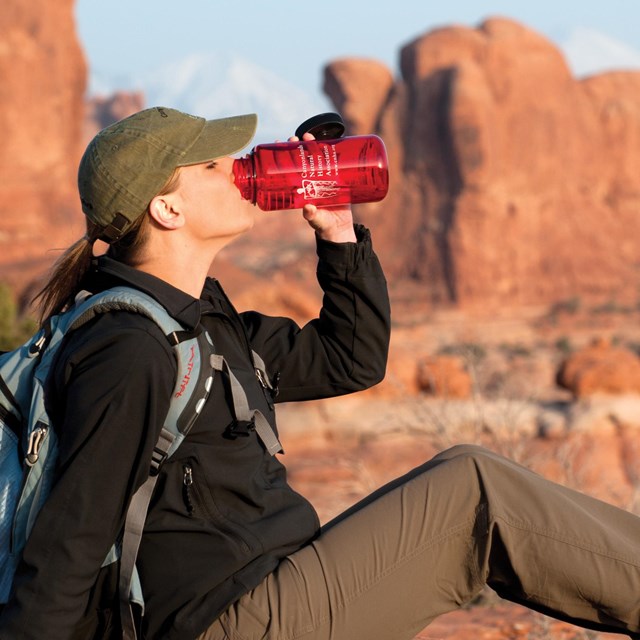 a woman drinks water from a red bottle