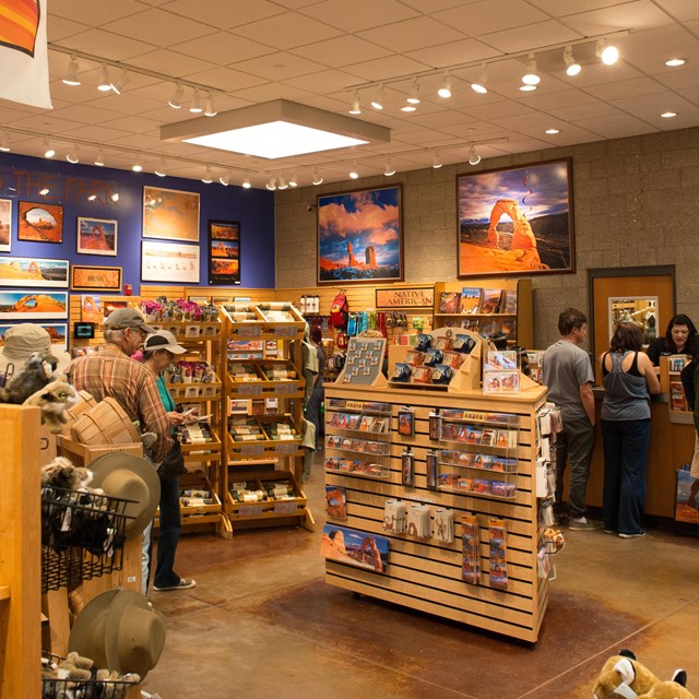 people walk around shelves in a bookstore. banners hang overhead with posters on the wall