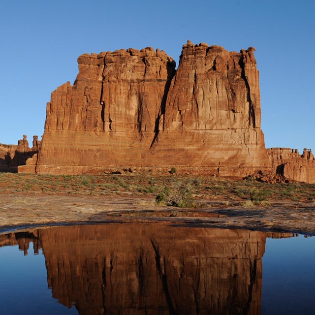 A giant rock monolith reflected in a still pool of water in the foreground