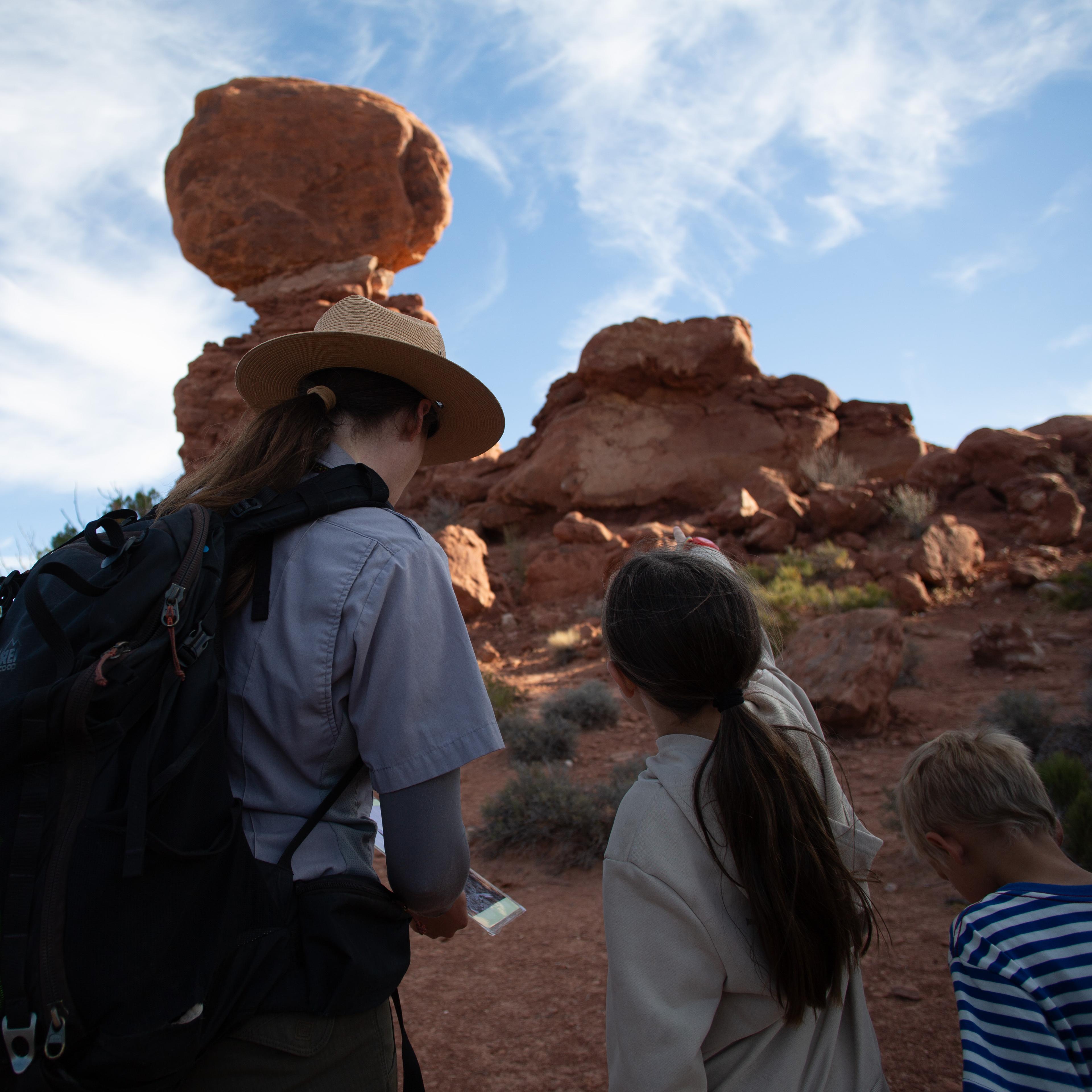 A ranger and student stand in front of a large sandstone feature