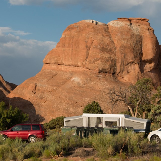 a pop-up trailer and two vehicles in front of red rock cliffs