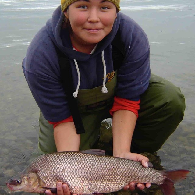 A young woman holds a whitefish she harvested.