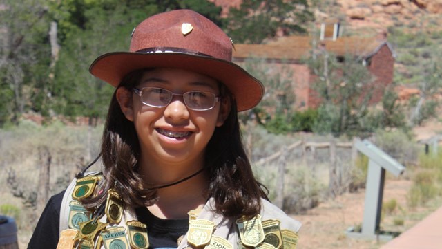 junior ranger wearing NPS flat hat and vest filled with junior ranger badges