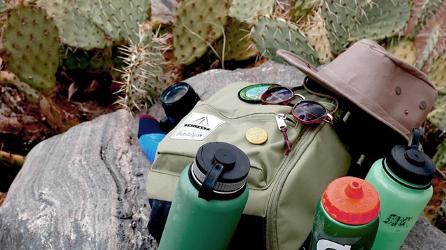 Hiking gear in a pile, including a backpack, water bottles, and sunglasses