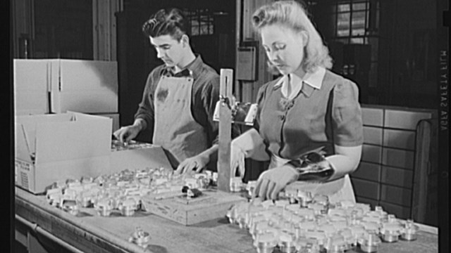 A man and woman in work clothes work at a table