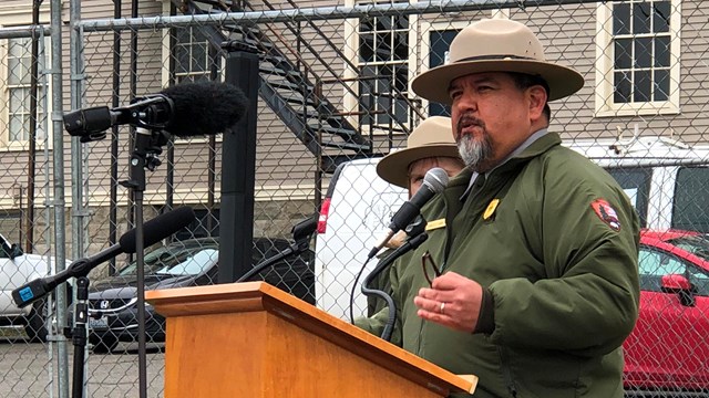 A man in a National Park Service uniform speaks at a podium.