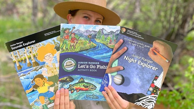 Park ranger holds Sound Explorer, Junior Angler, and Night Explorer books