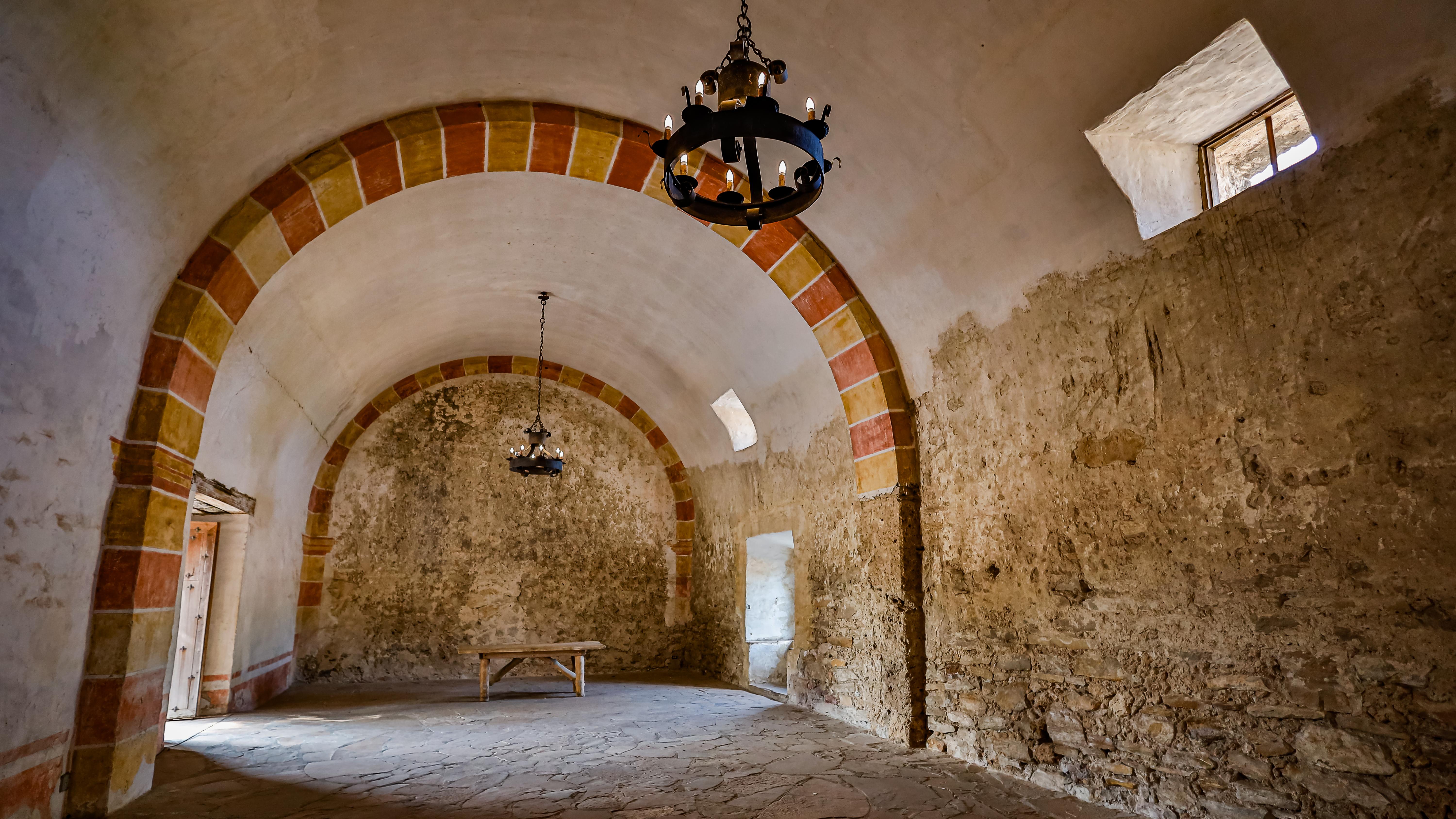 Arched room with two chandeliers hanging from ceiling, a sky light, and exposed stone walls