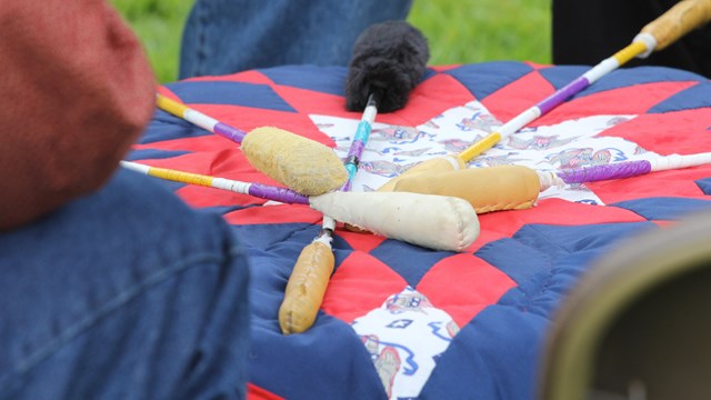 A photo of drumsticks resting on a colorful quilt.