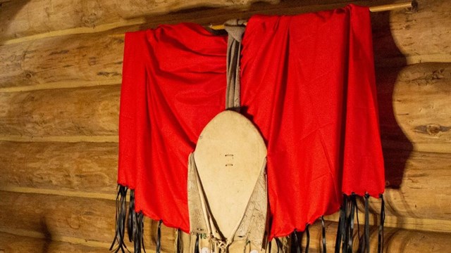 Red Shawl draped over on a traditional dress hanging on the wall above a bed