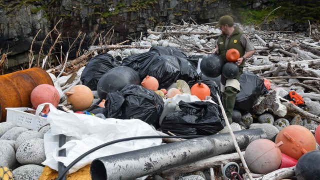 A ranger stands next to a large pile of trash on a beach
