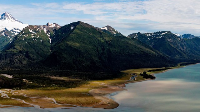 Aerial view of a coastal bay with snow-capped mountains rising from the water's edge.