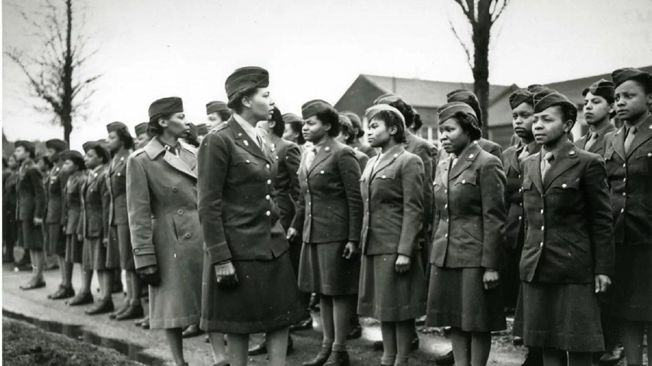 African American women wearing military uniform stand in formation while two other women inspect