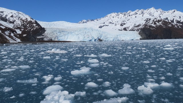 A wide vista of icy water with a tidewater glacier and mountains beyond