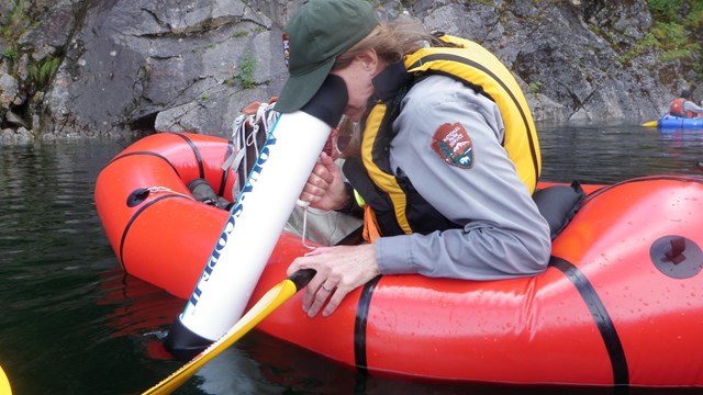 A ranger in a packraft looks through a lens into the water