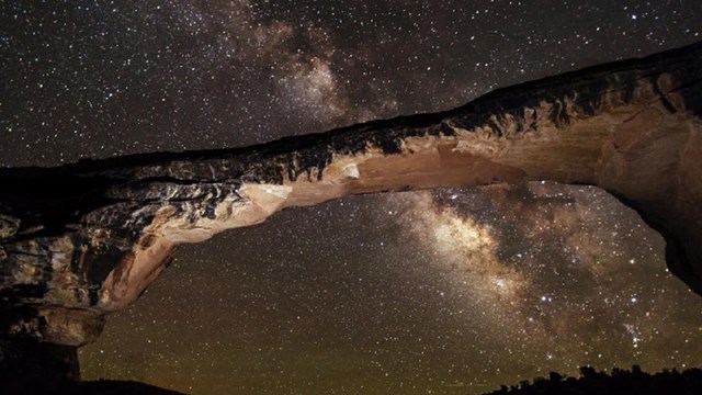 A stone arch in front of the Milky Way in the night sky.