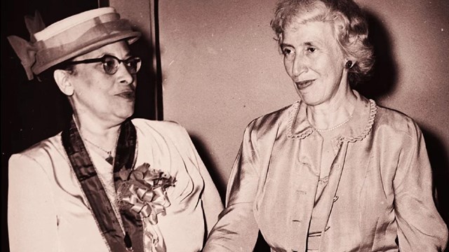 An African American woman and a white woman, both middle aged, shake hands