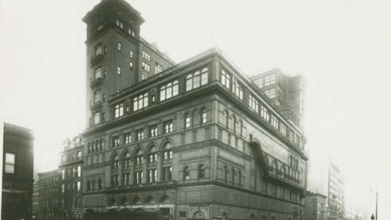 Black and white photo of exterior of large stone building. Public domain. 