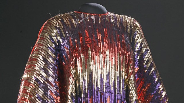Red, gold, and blue sequin dress designed with horizontal, varied stripes and large open sleeves.