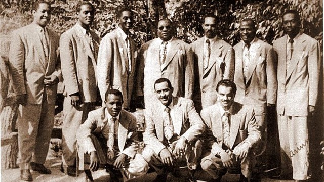 Ten band members pose in suits. Five are kneeling and five are standing.