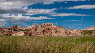 looking up from prairie grasses, jagged badlands buttes stretch into a cloudy blue sky