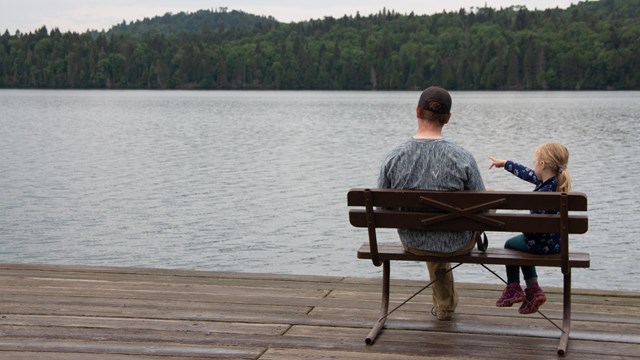 A father and daughter sitting on a bench looking out to Washington Harbor.