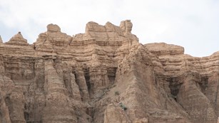 tan badlands buttes reach up into a cloudy, grey sky
