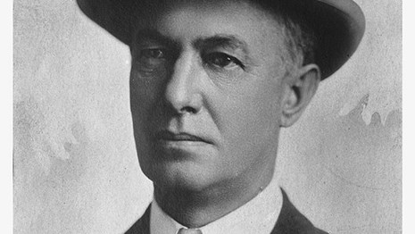 Black and white photo of a man in suit and tie with hat