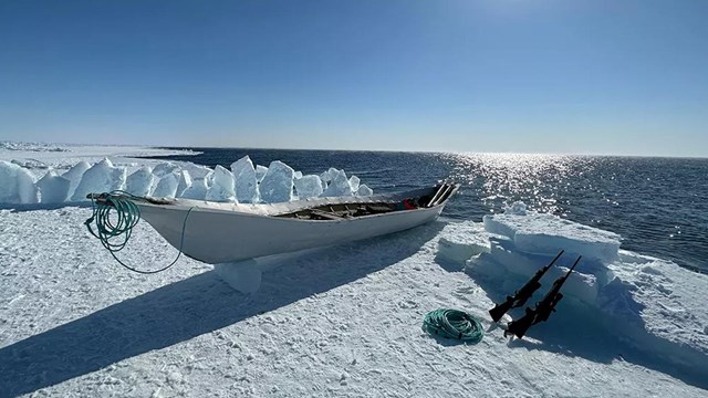A boat and hunting rifles on ice next to ocean