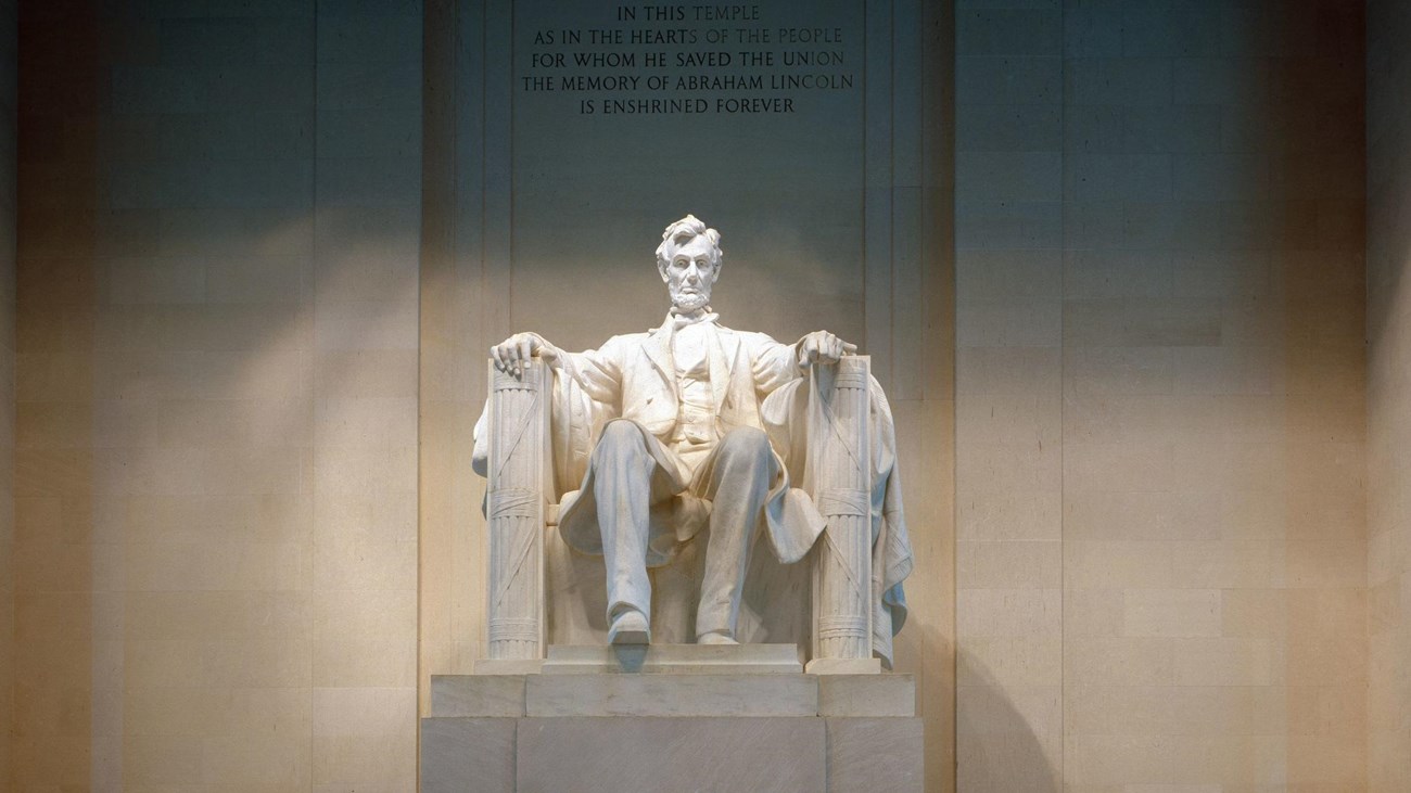 A large carved statue of President Lincoln sits in a chair within the Lincoln Memorial. 