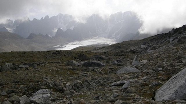 Landscape view of a cloudy day, mountains, and a rocky field.