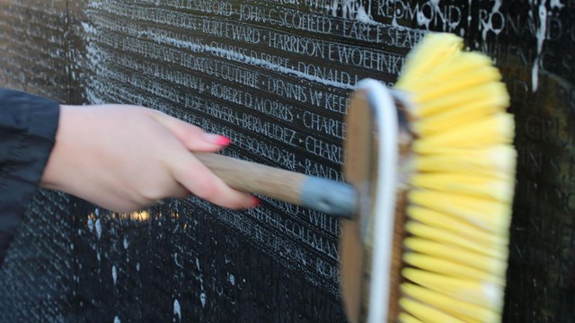 A volunteer uses a cleaning brush to scrub the wall of names at the Vietnam Veteran’s Memorial