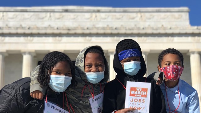 Students  with mask pose with voting rights cards in front of the Lincoln Memorial