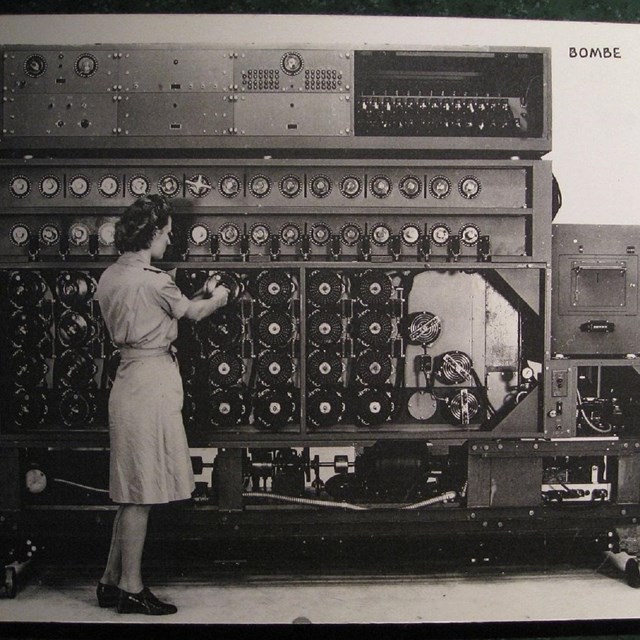 A woman stands in front of a large machine with several knobs and dials