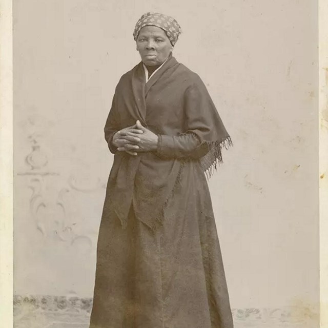 African American woman wearing black dress and shawl and patterned headscarf with hands folded