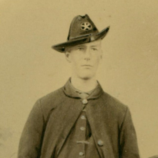 Studio portrait of two young men in Civil War uniforms with painted camp backdrop