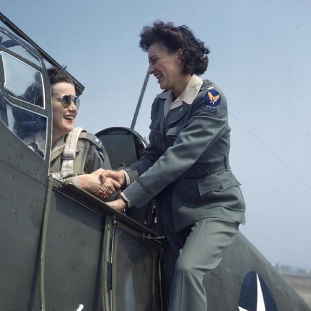 Two woman speak as one is seated in the cockpit of a plane