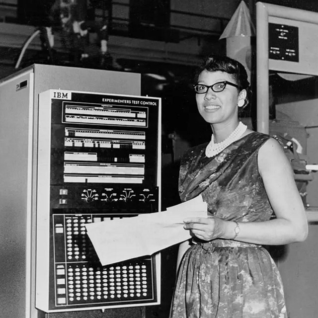 woman in 50s dress in front of an old IBM computer