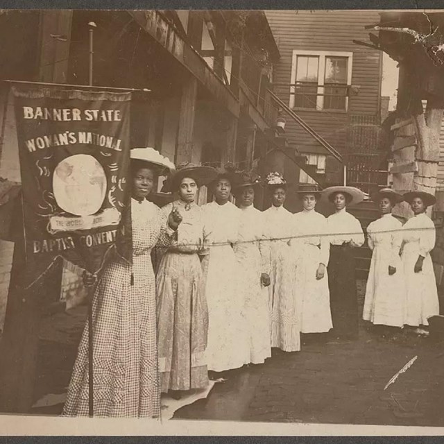 A group of women in victorian dress holding a banner