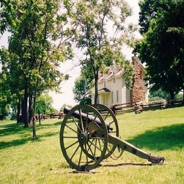 Civil War era cannon on green lawn in front of a two story white house surrounded by trees