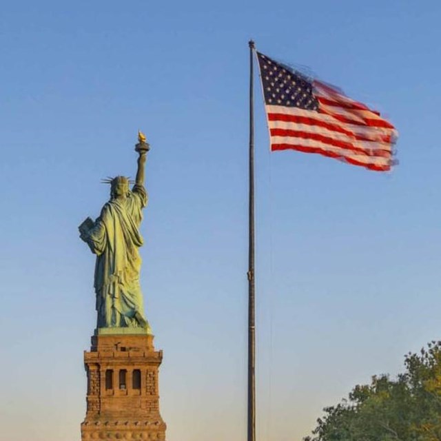 Photograph of the Statue of Liberty and American flag on pole at sunset