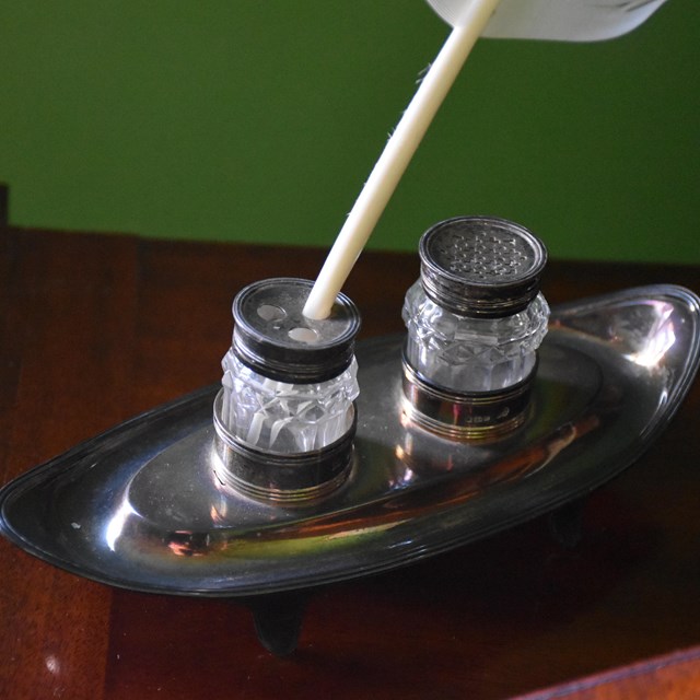 A silver-plated inkstand with a feather in it.