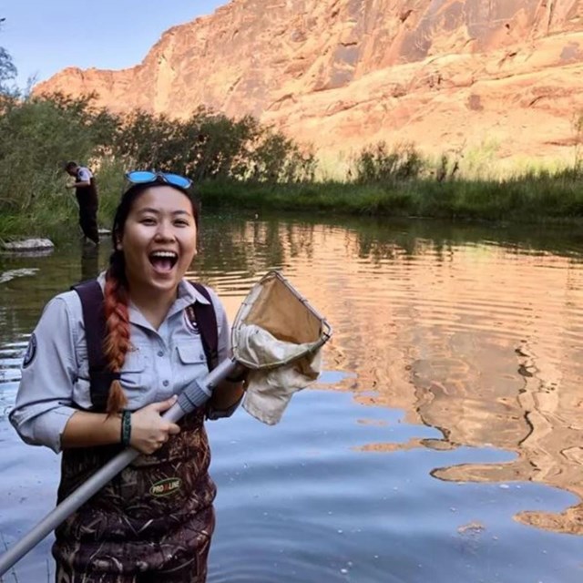 A smiling young woman in national park service uniform holds a net