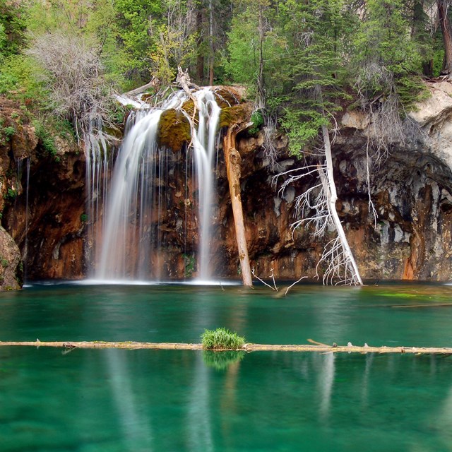 a waterfall flows into an emerald green clear pool