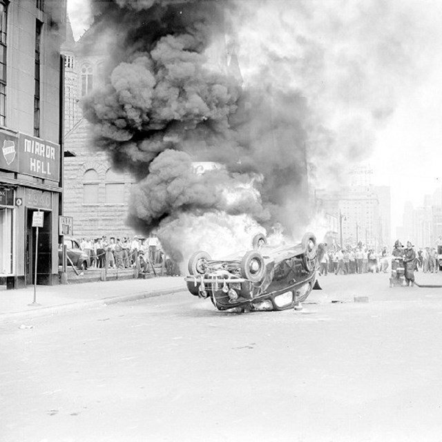 An old style of car lays upside down billowing smoke