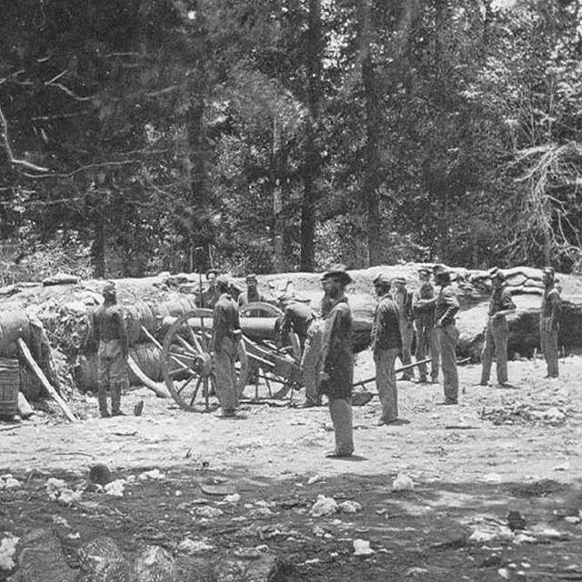 Men standing in a field around a cannon in Civil War uniforms