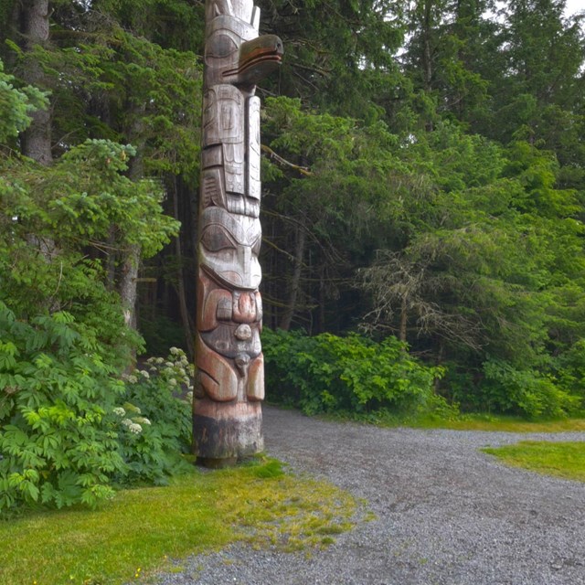 Photograph of totem pole next to pathway into green forest